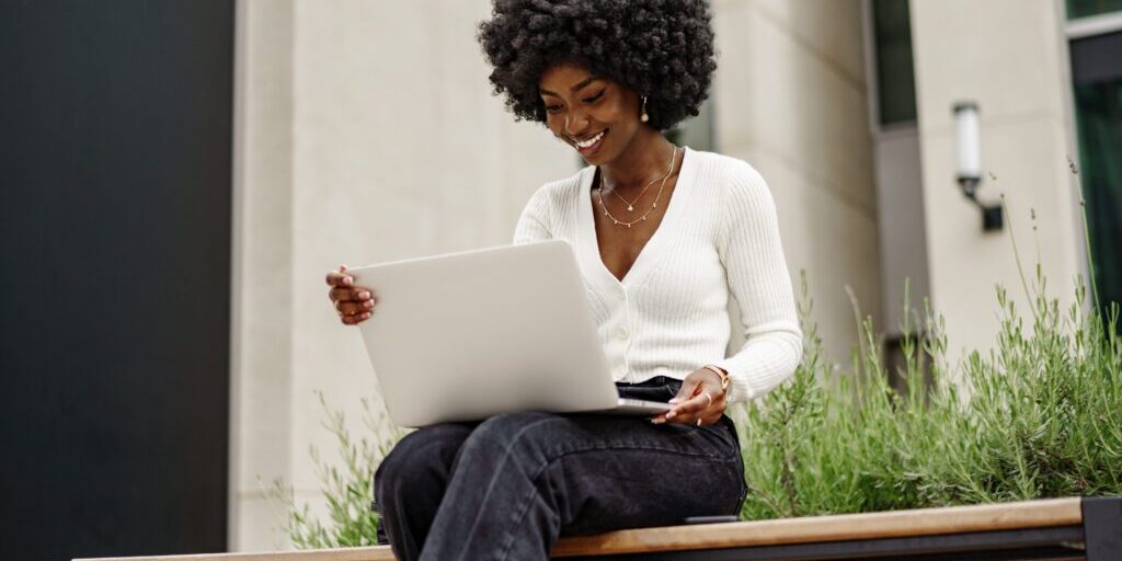 Young African American businesswoman working using laptop sitting on the bench in the city, close up